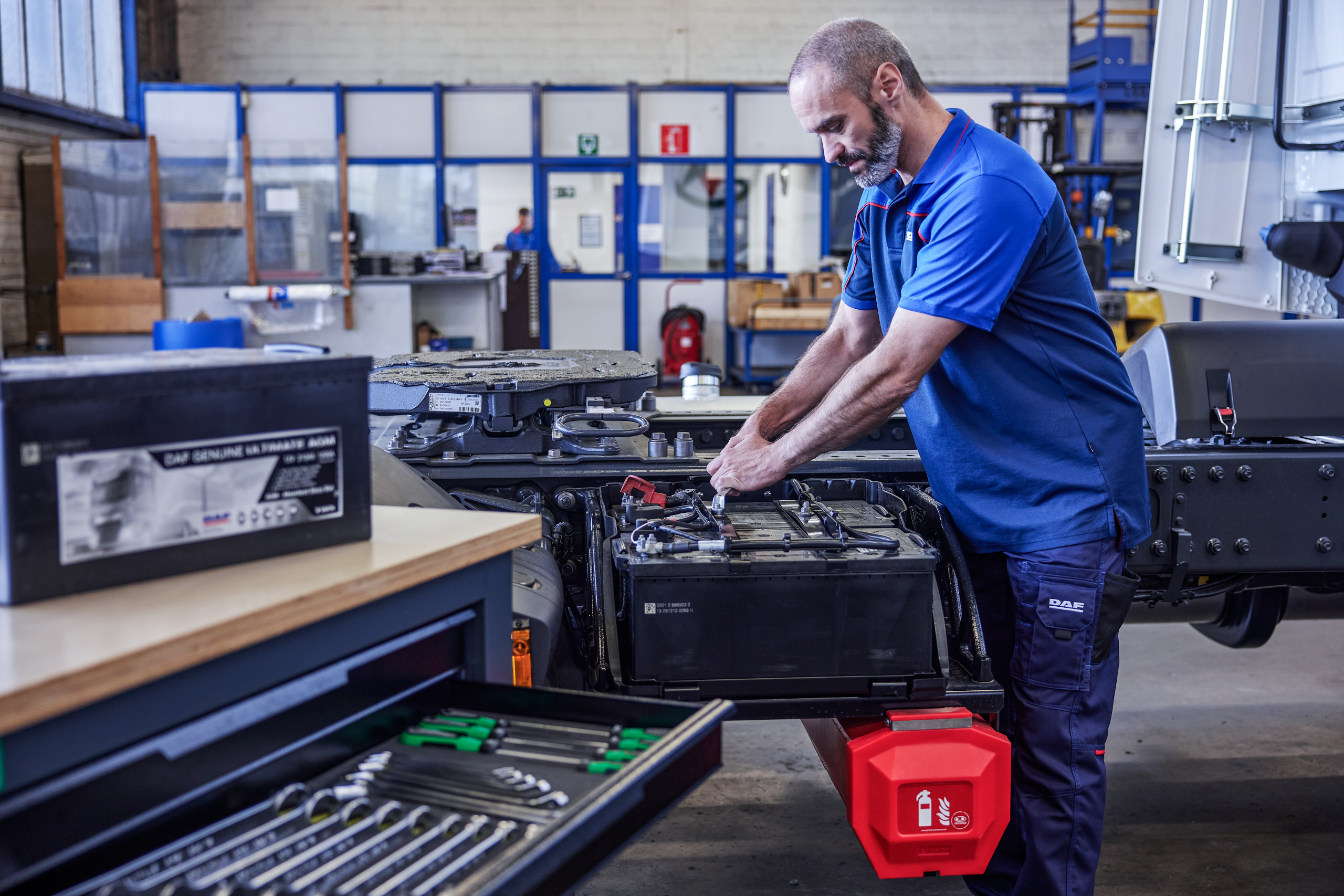 DAF mechanic installing a battery in a truck chassis inside a workshop